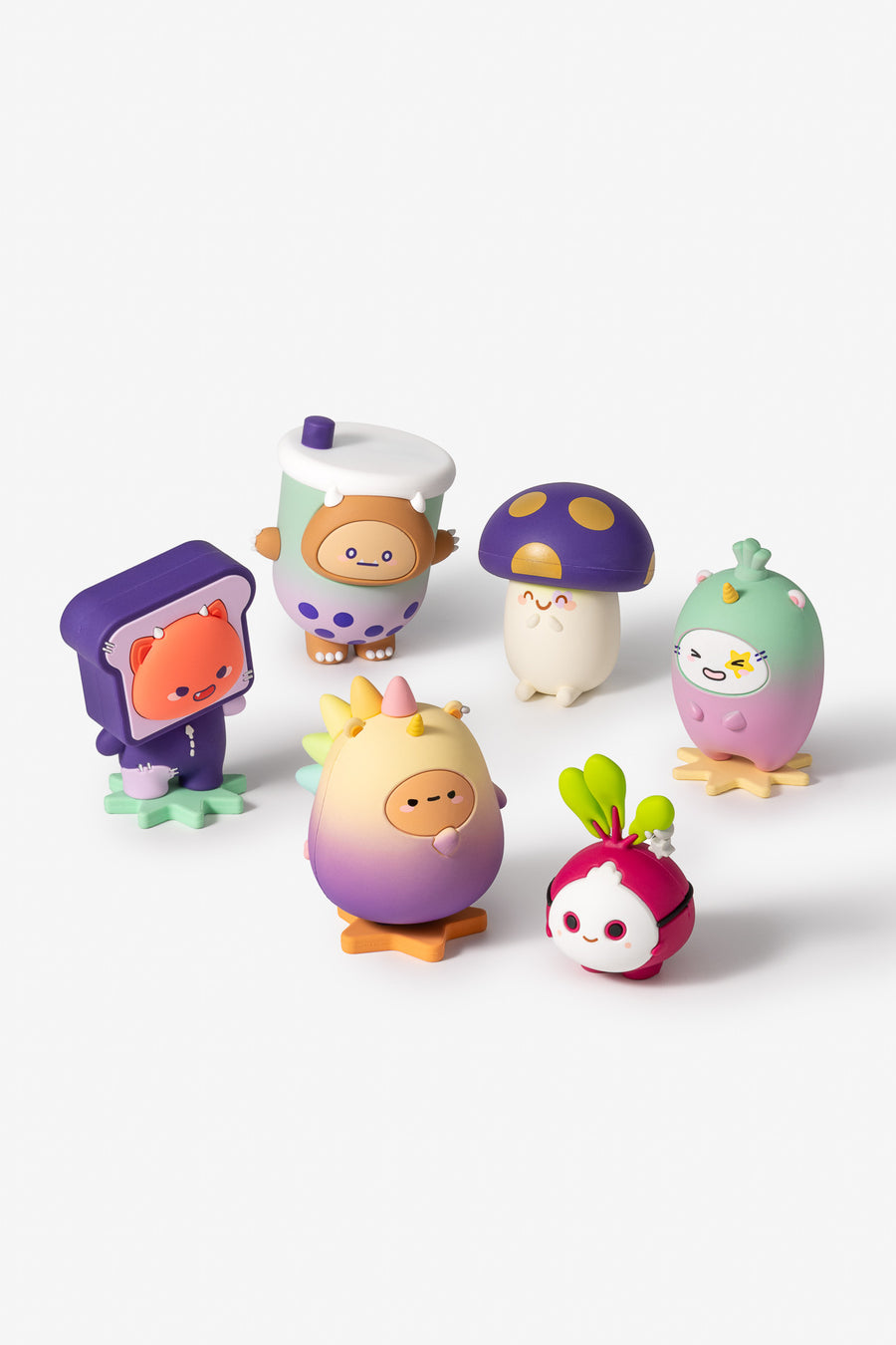 A set of six cute, colorful character figurines arranged on a clean white studio background. The characters include a toast-shaped figure with an orange cat face, a cup-shaped figure with a brown bear head, a mushroom figure, a green-and-pink bird figure, a yellow-and-purple bird figure, and a radish-like figure with green leaves.