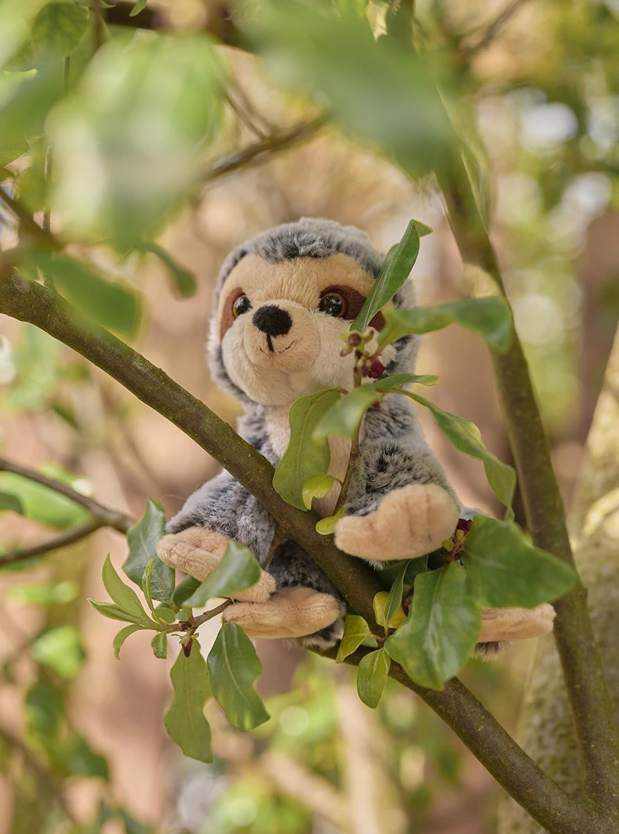 Plush sloth toy in a tree with green leaves