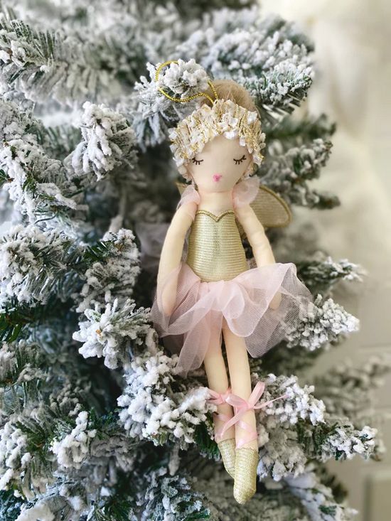 A plush ballerina doll with a gold bodice, pink tutu, and golden ballet shoes hangs on a snow-covered Christmas tree.
