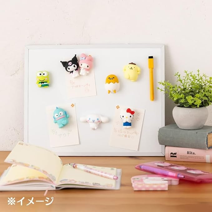 White whiteboard with Sanrio character magnets, yellow marker, notebook, stationery, potted plant, books.
