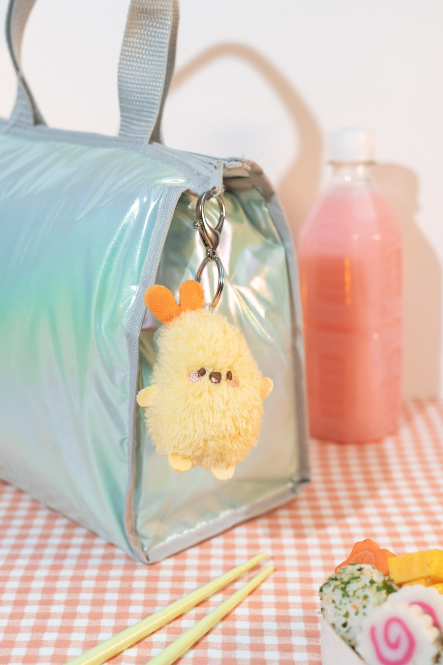 Light blue bag with a fluffy yellow keychain on a checkered tablecloth.