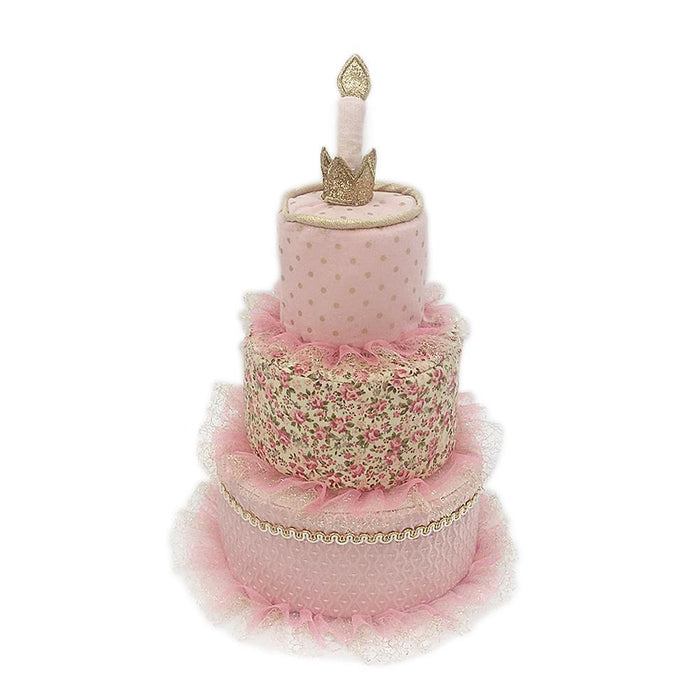 Three-tiered pink fabric cake with floral and polka dot patterns, gold trim, and a candle.