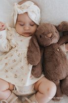 Sleeping baby with floral headband and dress, bunny stuffed animal, knit socks.