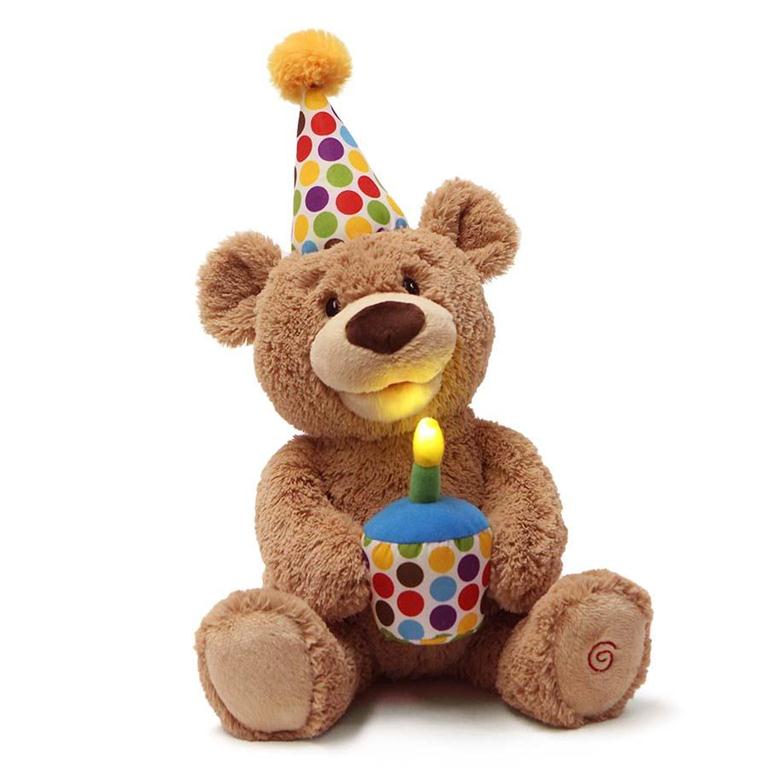 Brown teddy bear wearing a colorful polka-dot birthday hat and holding a cupcake with a lit candle.