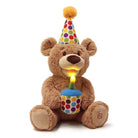 Brown teddy bear wearing a polka dot party hat and holding a lit birthday candle cupcake.