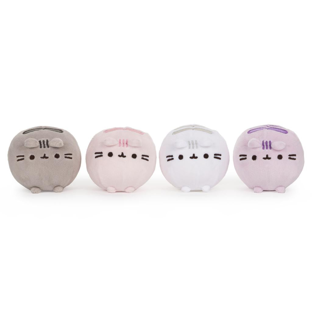 Four small, round, plush cat toys in gray, pink, white, and purple, arranged in a row.