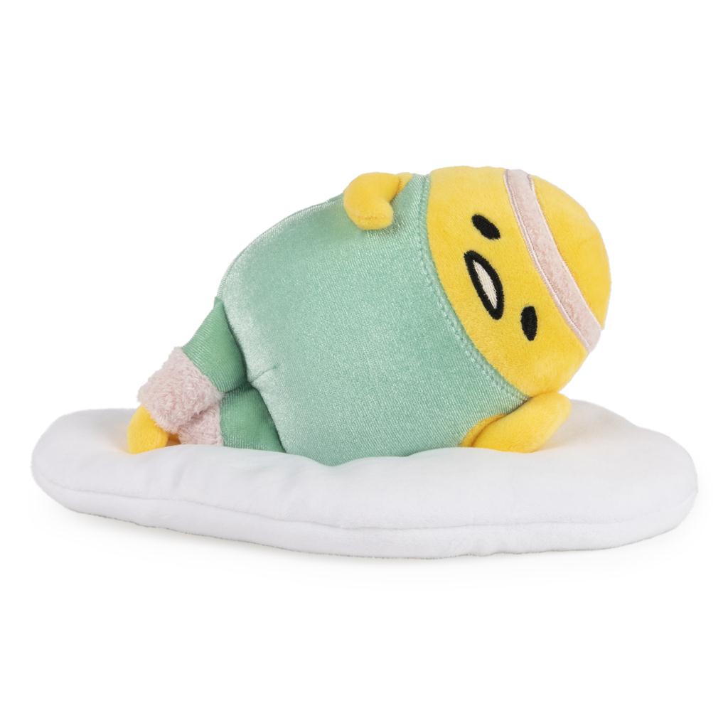 Stuffed toy egg character in green pajamas lying on a white pillow.