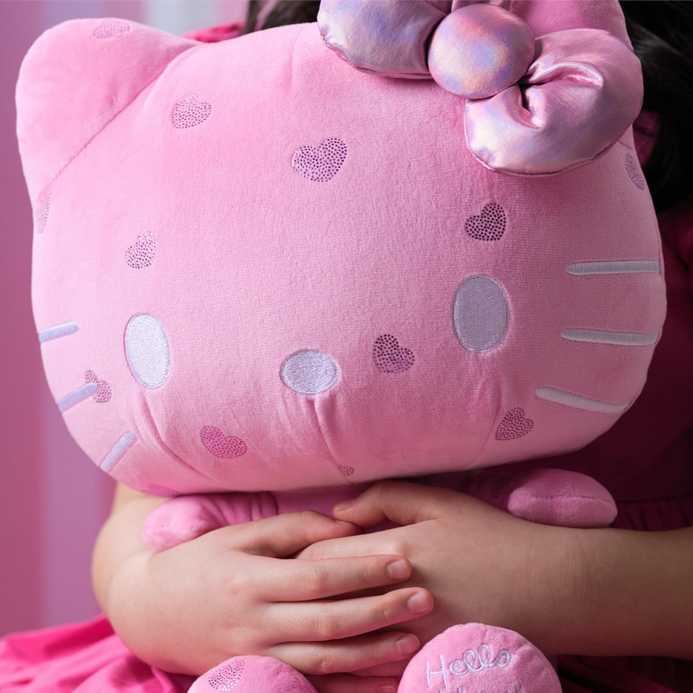 A person holding a pink Hello Kitty plush with heart details.