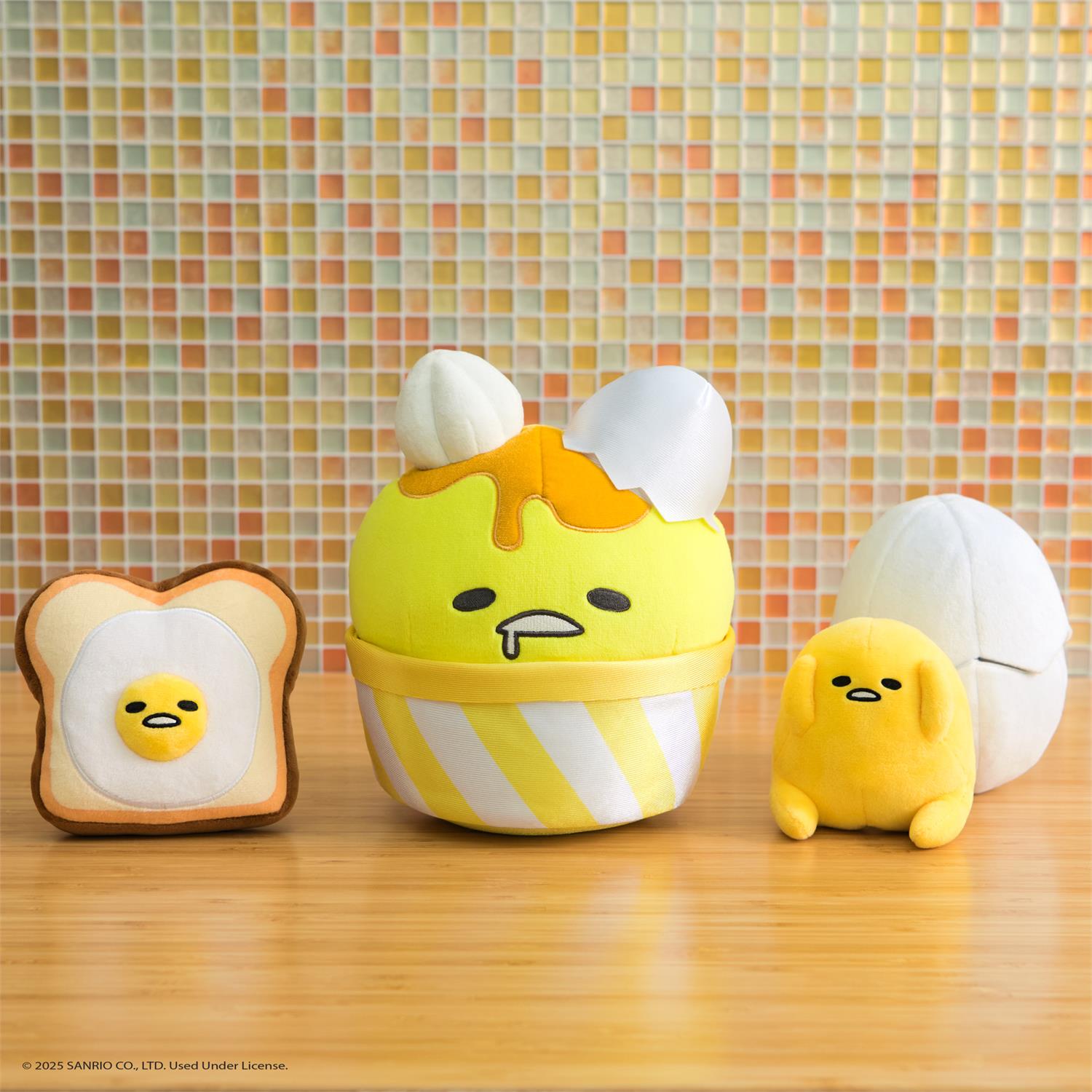 Four Gudetama-themed plush toys arranged on a wooden surface against a colorful tiled wall.