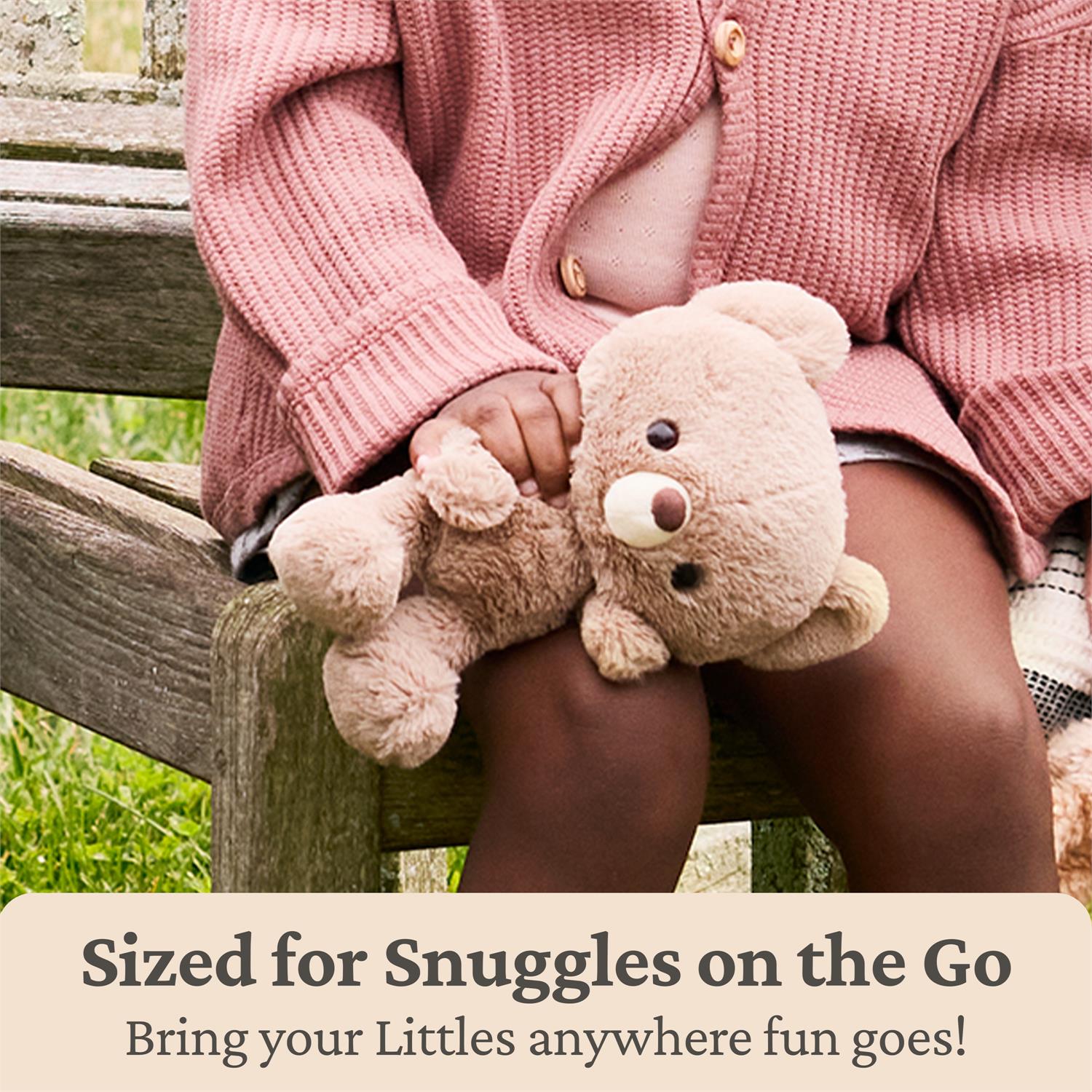 Child on wooden bench wearing pink sweater, holding brown stuffed teddy bear.