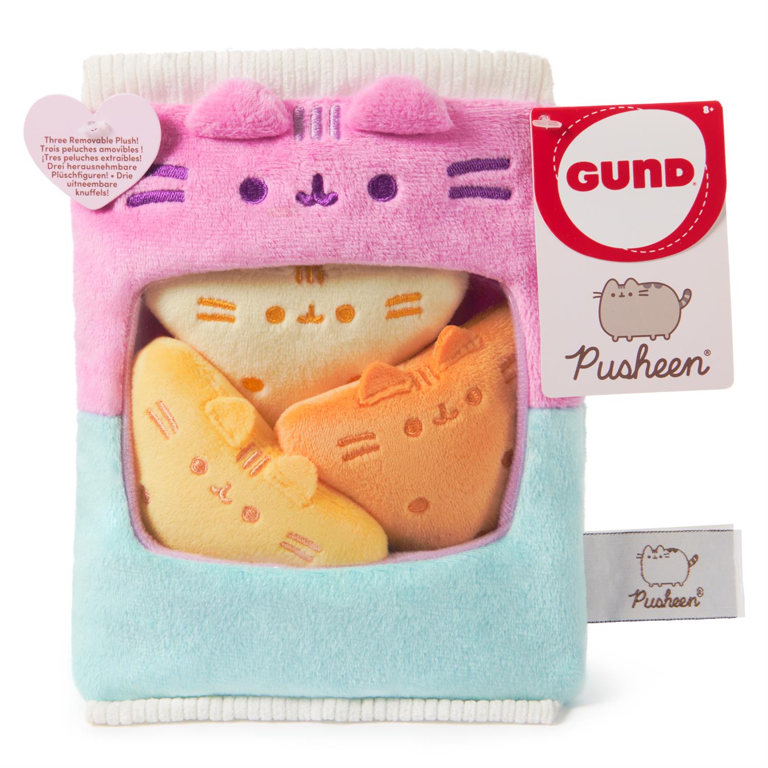 Pink and blue Pusheen plush toy in a box, with three removable cat-shaped plushies inside. A tag with the Gund logo and Pusheen's name is attached.