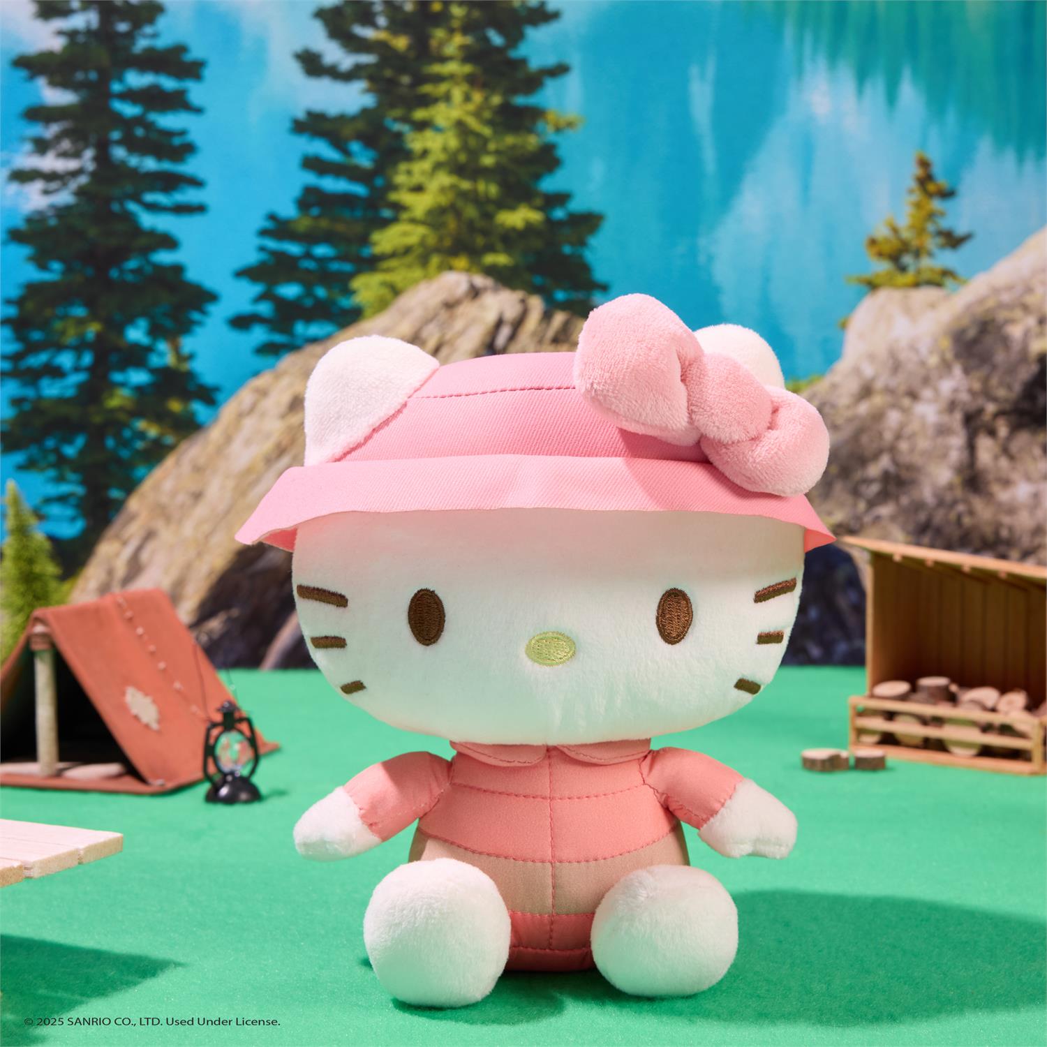 Hello Kitty plush toy wearing a pink raincoat in a forest setting with trees and rocks.