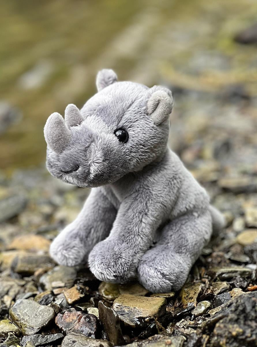 Plush rhino toy on a rocky surface with water in the background