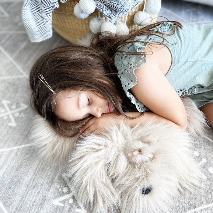 A child is sleeping on a fluffy pillow while lying on a patterned rug next to a basket filled with fabric.