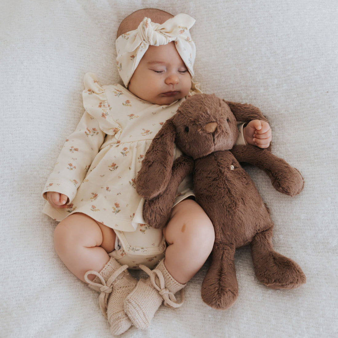 A baby girl sleeping with a stuffed bunny.