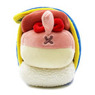 Plush toy of a character with pink face and red eyes, a brown 'nose', and a stitched 'X' on its face. It's surrounded by yellow and blue trim, resting on a fluffy white base.