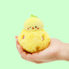 Plush toy resembling a yellow chick held in a hand against a light green background