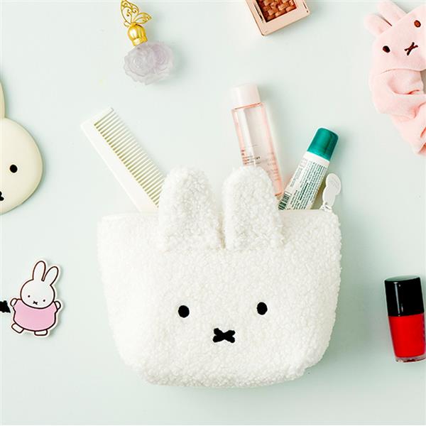 A fluffy white bunny pouch filled with makeup, hair accessories, and skincare products, surrounded by additional beauty items.