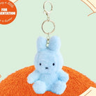 Light blue plush bunny keychain with silver hardware, resting on an orange fuzzy surface.