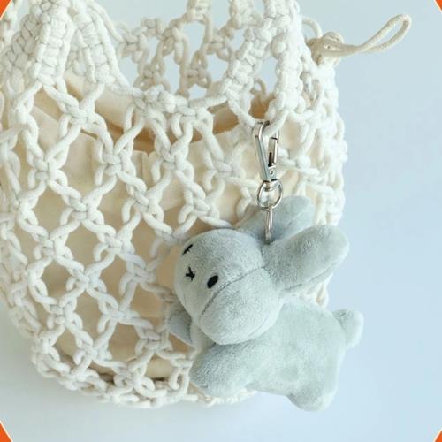 Close-up of a crocheted tote bag with a gray plush bunny keychain attached.