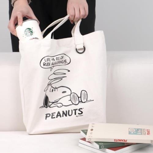A person putting a coffee cup into a white canvas tote bag featuring Snoopy and the words "Life is full of rude awakenings."