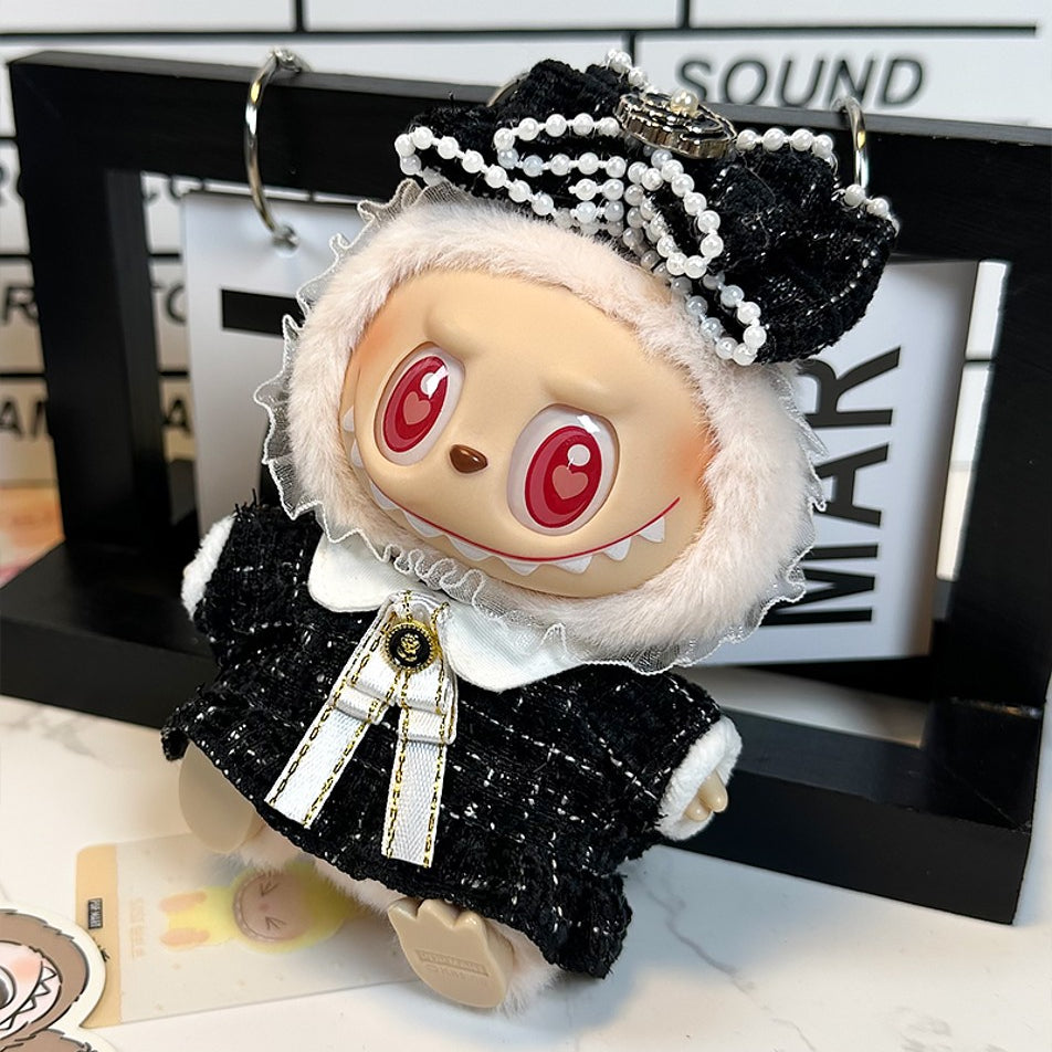 Close-up of a doll dressed in a black and white tweed outfit with a large bow and pearl embellishments. The doll has red heart-shaped eyes and a toothy grin.