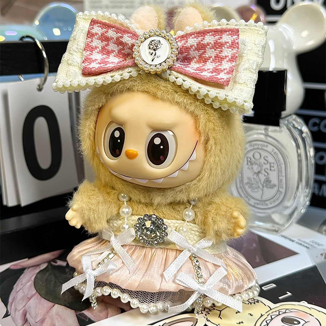 A doll wearing a fuzzy hoodie with a pink bow, a pearl necklace, and a pink dress with bows.