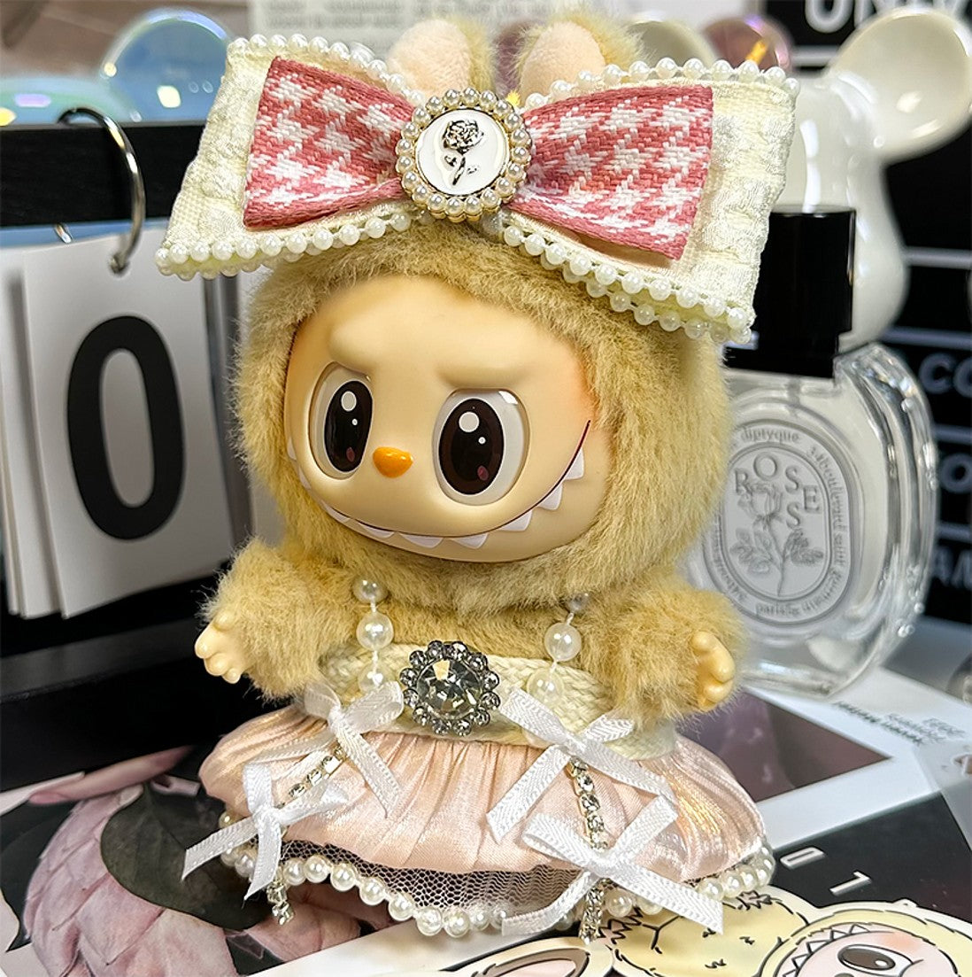 A doll wearing a fuzzy hoodie with a pink bow, a pearl necklace, and a pink dress with bows.