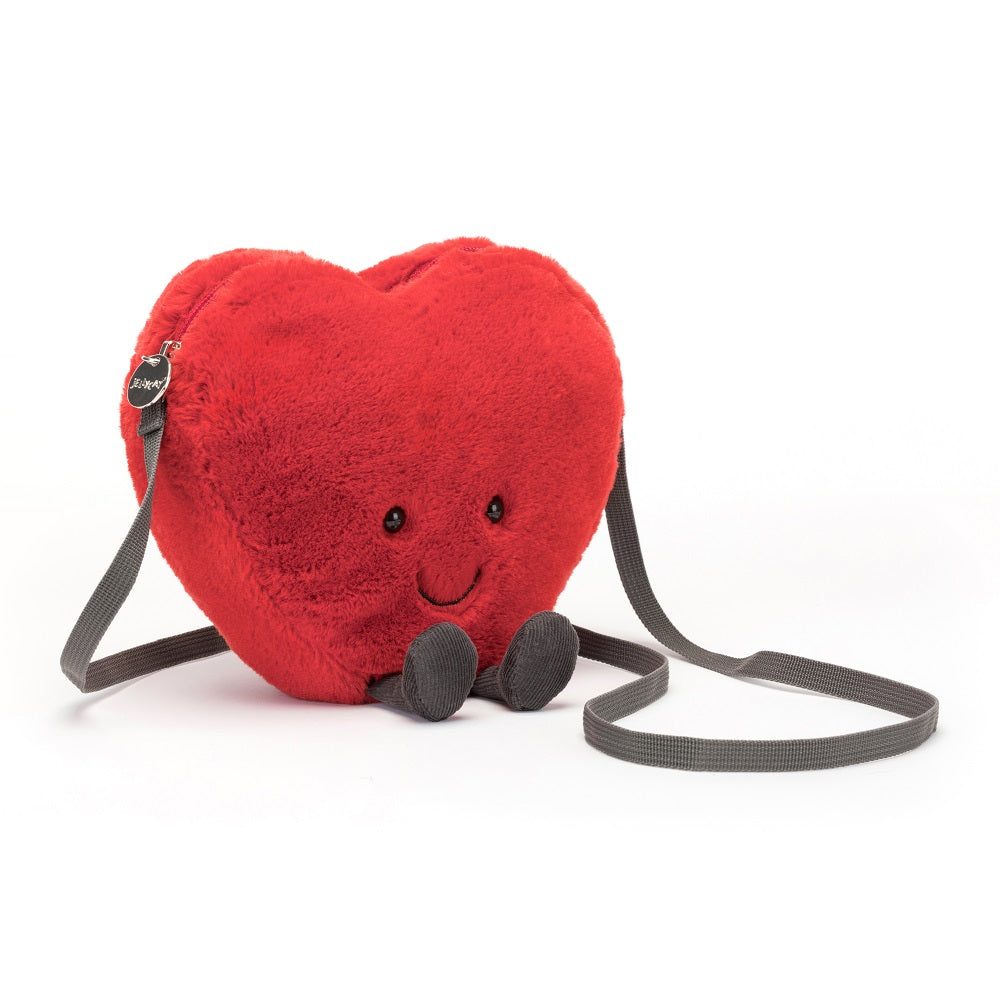 Plush red heart-shaped purse with gray strap, eyes, smile, and legs.