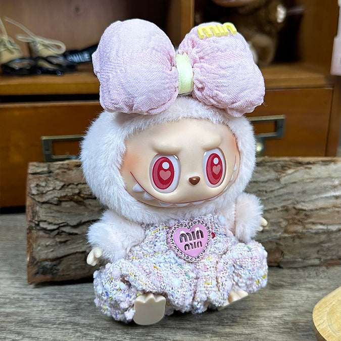A collectible toy figure with a large pink bow, furry white trim, heart-shaped eyes, and a tweed dress.