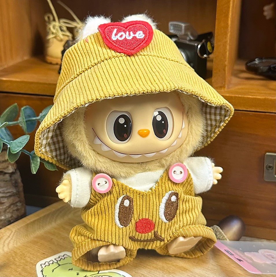 Stuffed doll wearing a yellow corduroy bucket hat with a red heart, matching corduroy overalls with a whimsical face, and a white shirt.