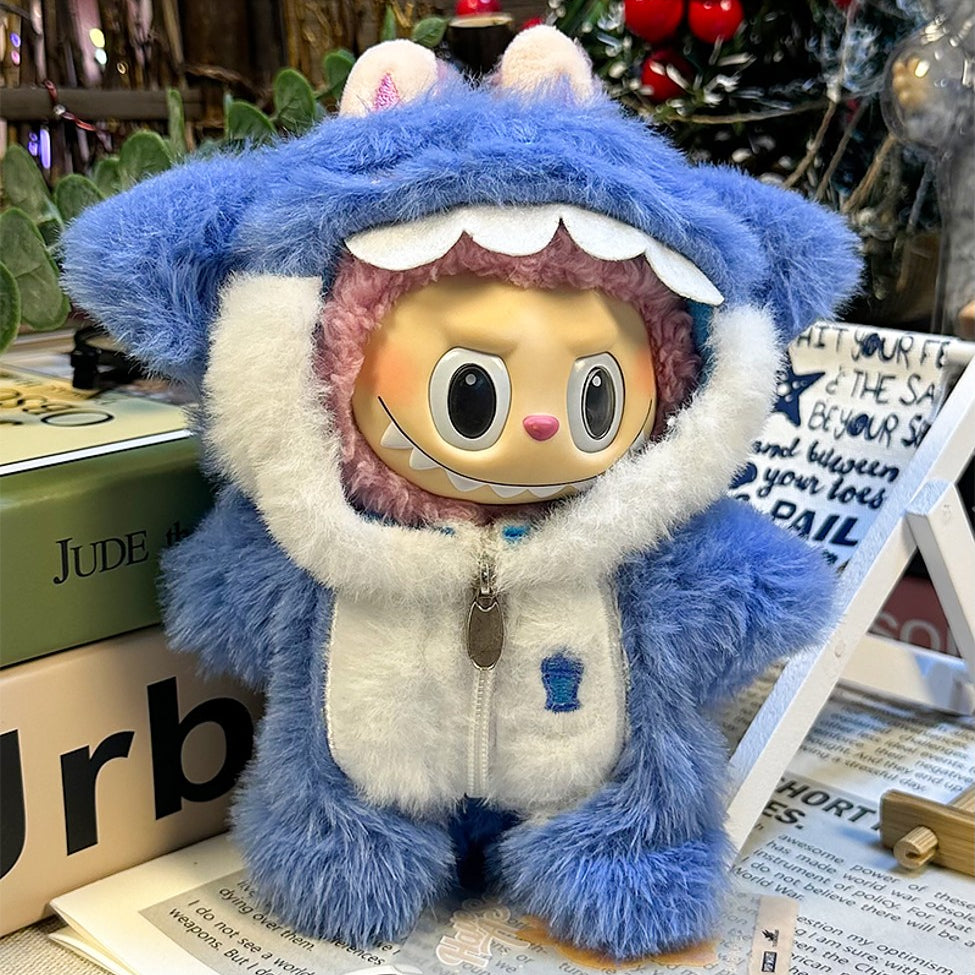 A doll in a blue furry shark costume with a white zipper and hood, resting on a newspaper and books.
