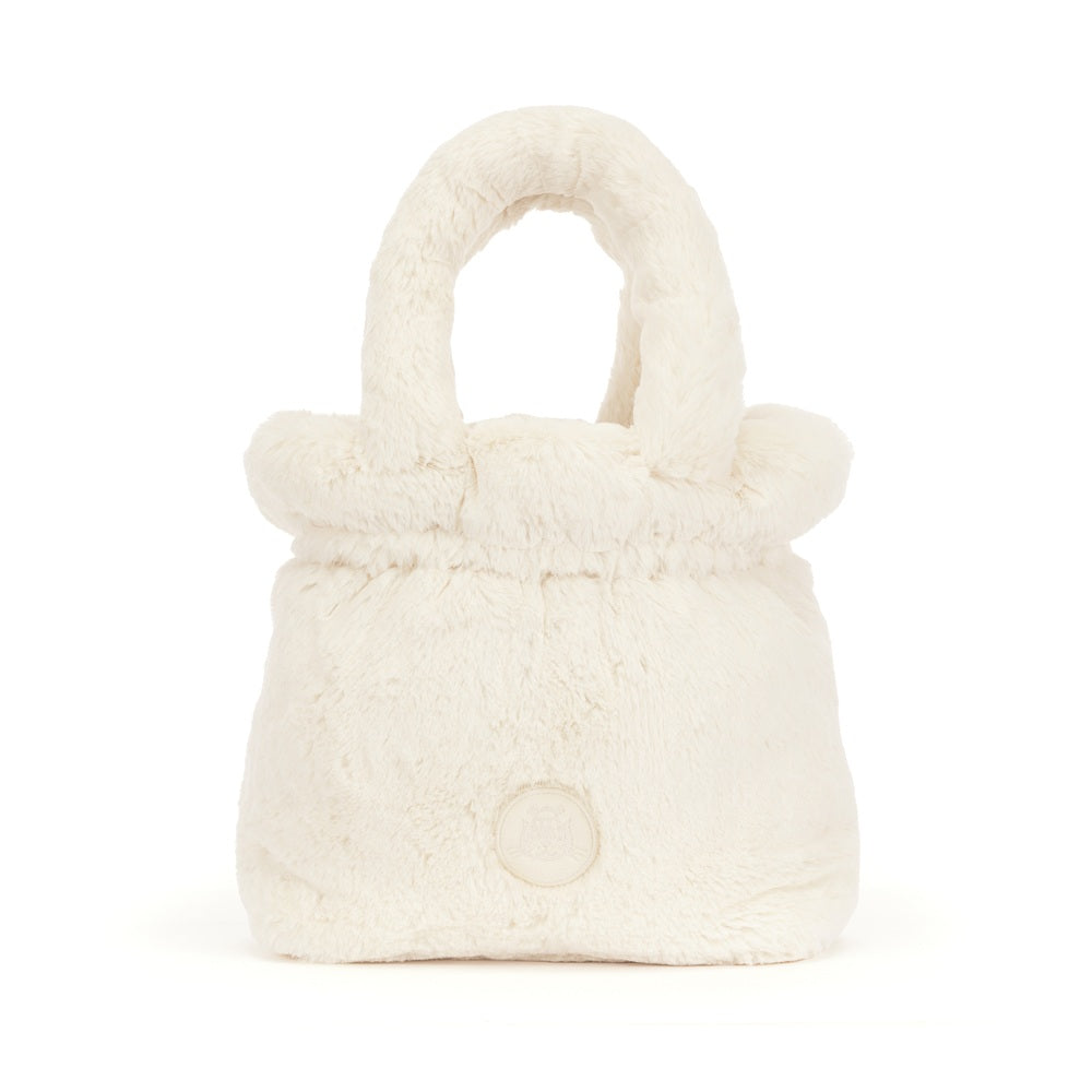 A small plush faux-fur handbag in a warm off-white or cream color, featuring a rounded top handle and a circular button detail on the front, set against a plain white background.