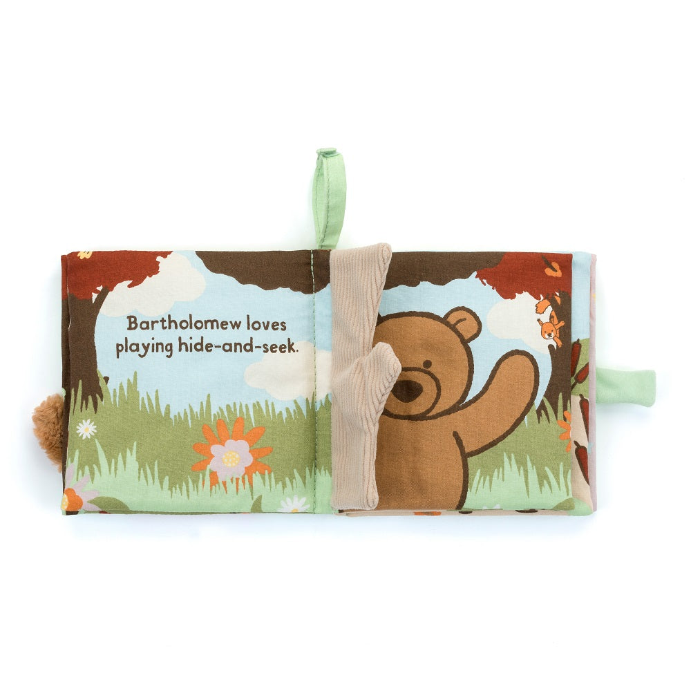 Open soft baby book with a brown bear, trees, flowers, and text "Bartholomew loves playing hide-and-seek."