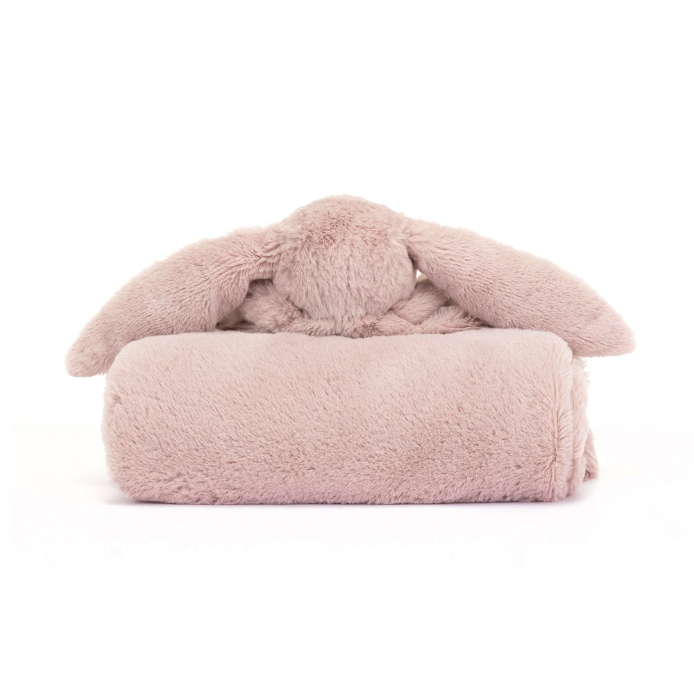 A plush, dusty pink bunny head with long floppy ears sits atop a rolled-up blanket of the same plush material and color.