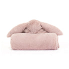 A plush, dusty pink bunny head with long floppy ears sits atop a rolled-up blanket of the same plush material and color.