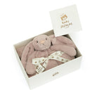 A blush-colored Baby Jellycat bunny toy in a white box with a white card and ribbon.