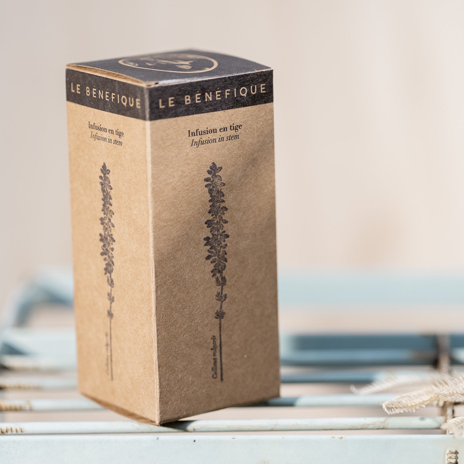 Tan product box with black top, featuring plant illustrations and bilingual text "Infusion en tige / Infusion in stem".