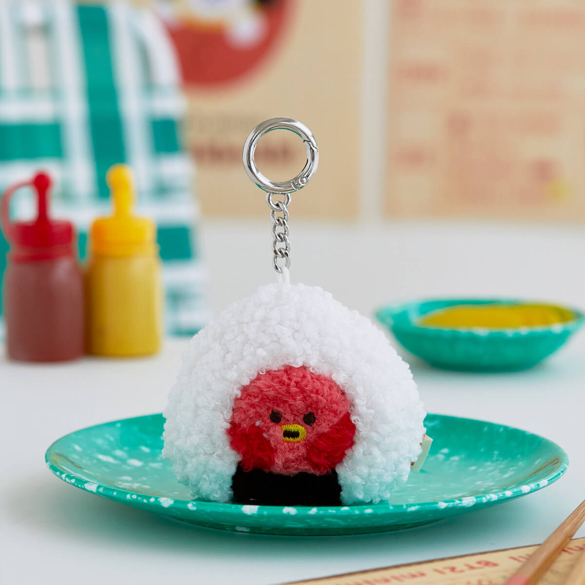 Cute onigiri keychain with red bird face on turquoise plate.