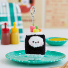 Sushi-shaped BT21 plush keychain on a speckled teal plate.