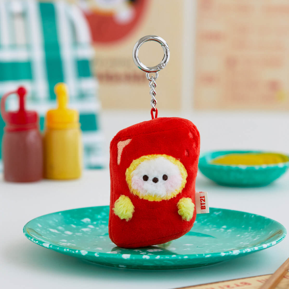 A plush BT21 Chimmy keychain in a red case sits on a speckled teal plate.