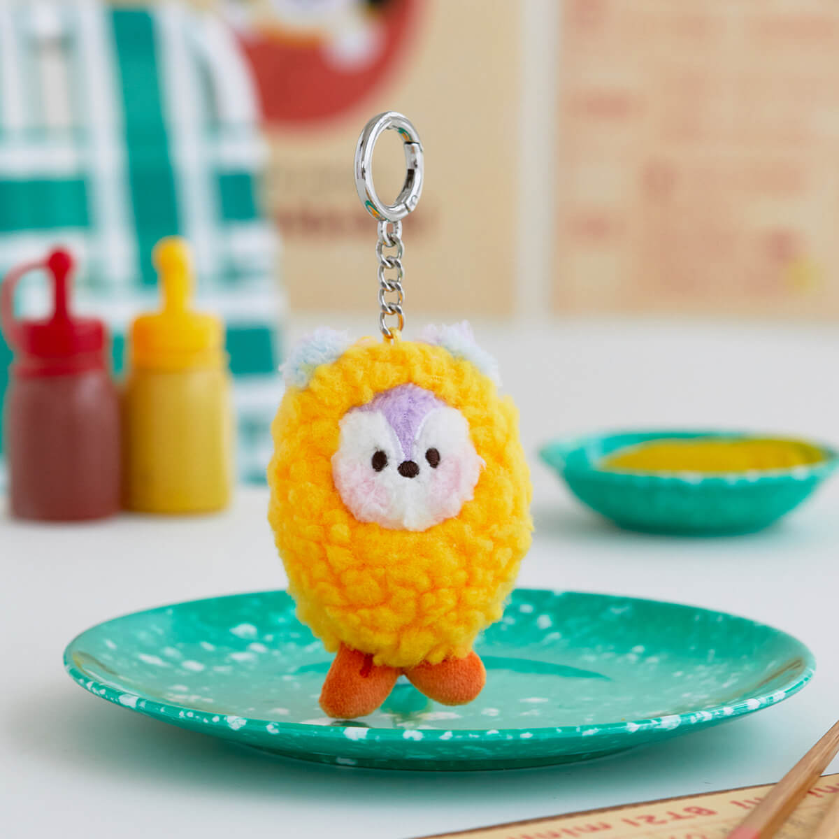Yellow plush keychain of a cartoon character on a teal speckled plate.