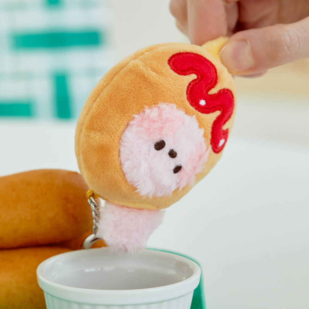 Plush hot dog keychain with pink furry face and red ketchup.