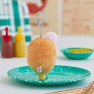Plush dumpling keychain on turquoise plate, silver ring and chain, pink puff, condiment bottles.