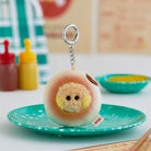 Plush BT21 character keychain on a speckled turquoise plate, with condiments and dishware in the background.