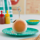 Plush BT21 bun keychain on a turquoise speckled plate, with bottles of condiments in the background.