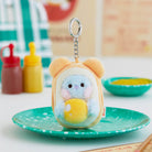 A blue and yellow BT21 character plush keychain with a silver clip, resting on a green speckled plate.