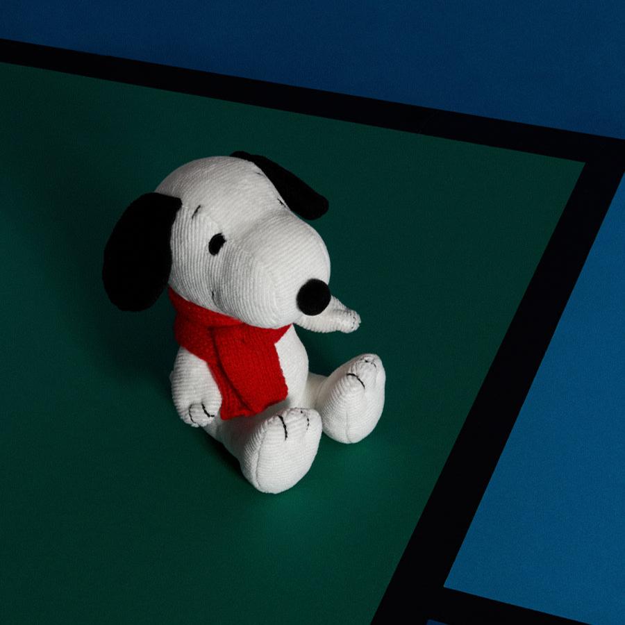 A Snoopy plush toy wearing a red scarf, sitting on a green and blue surface with black lines.