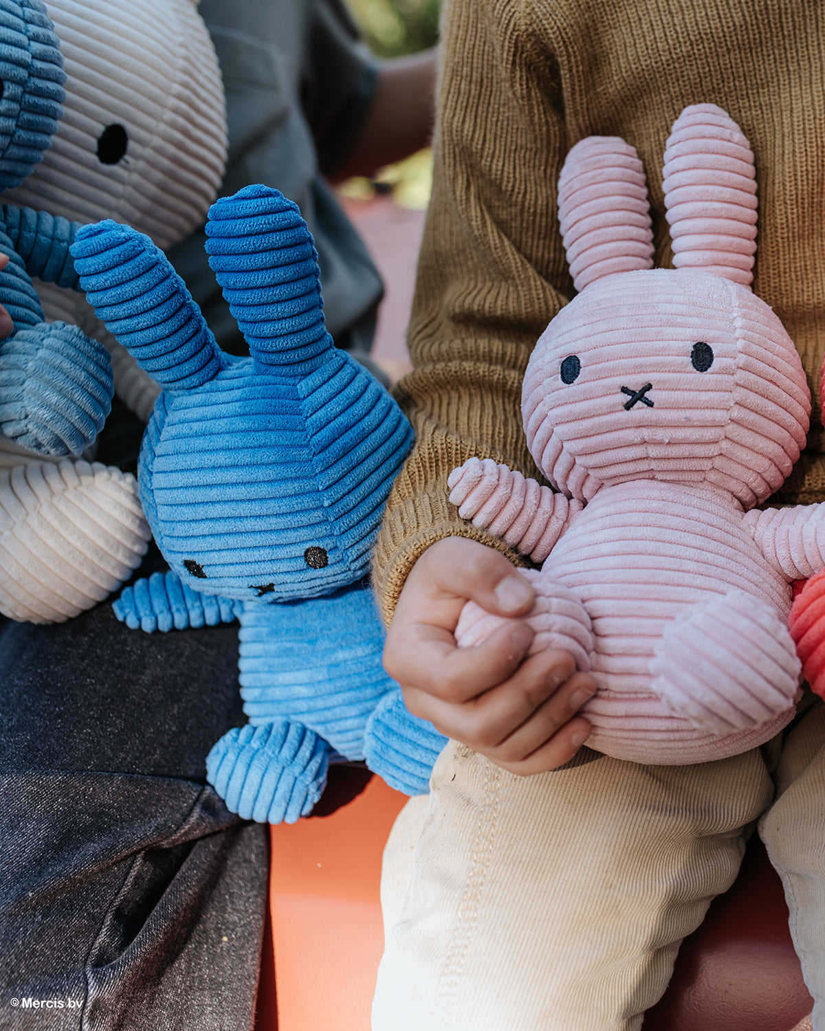 Corduroy bunny plush toys in blue, pink, and cream. Brown sweater and corduroy pants.