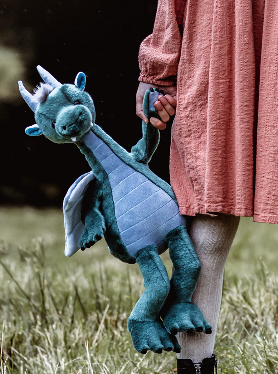 Person holding a blue dragon plush toy in a grassy field